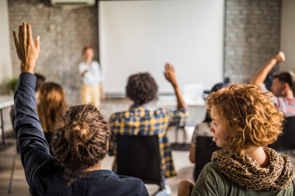 Back view of large group of people raising hands on a seminar in a board room. Back view of large group of people raising hands on a seminar in a board room.