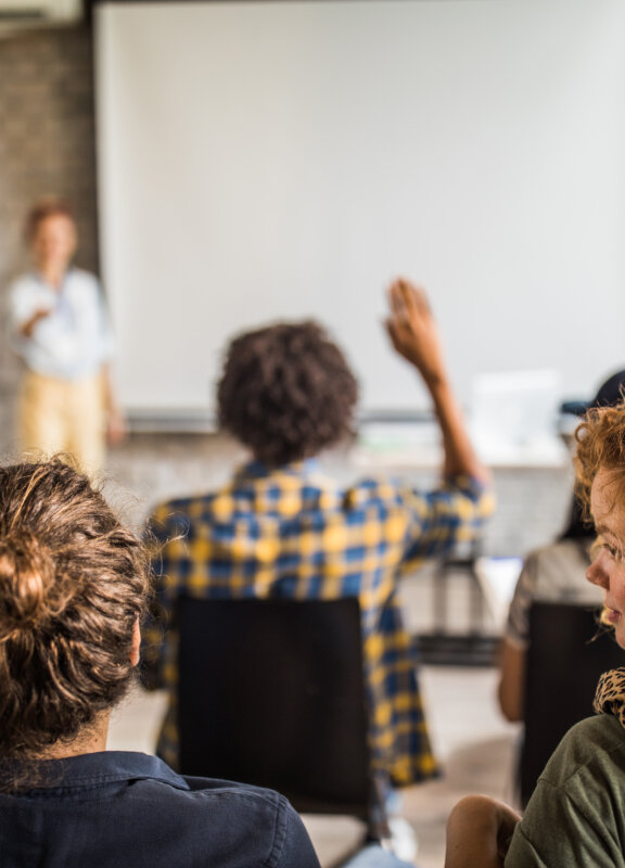 Back view of large group of people raising hands on a seminar in a board room.